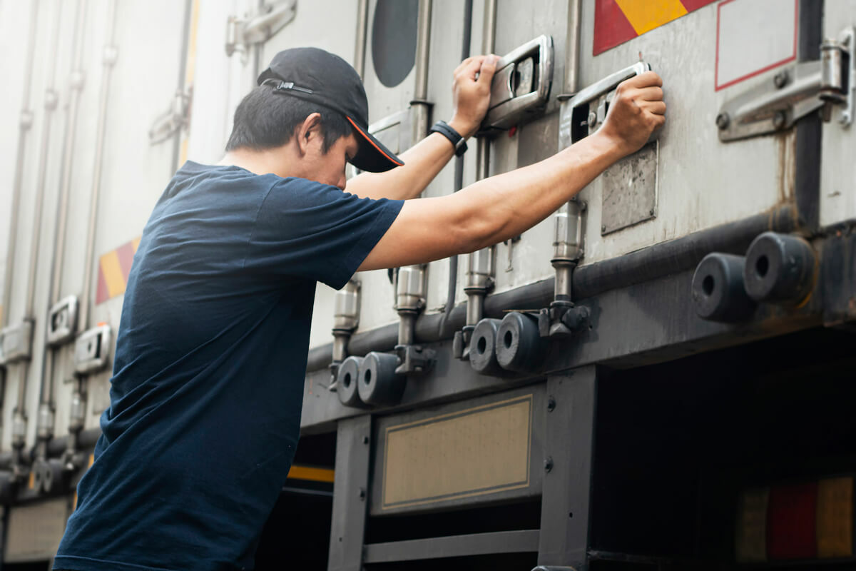 Exhausted truck driver leans against the back of his rig's trailer.