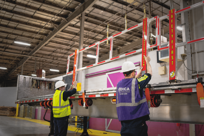 A photo of two men installing a Truck Fall Prevention Drop-In System on a flatbed trailer