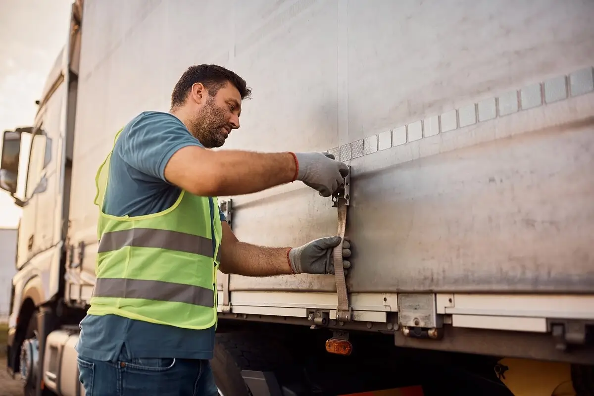 Truck driver tightening a tarpaulin on a flatbed trailer